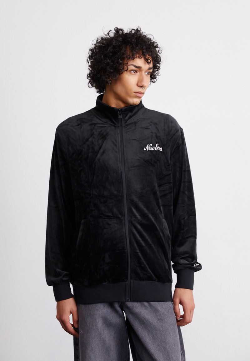 Sort velour zip-jakke med høj krave, der har sidelommer, elastiske manchetter og hvid broderet "New Era" logo på brystet.