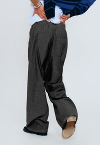 Pantalons en lin gris à jambes larges avec une texture simple et une taille élastique. Dotés d'une poche arrière ; associés à des chaussures sombres.