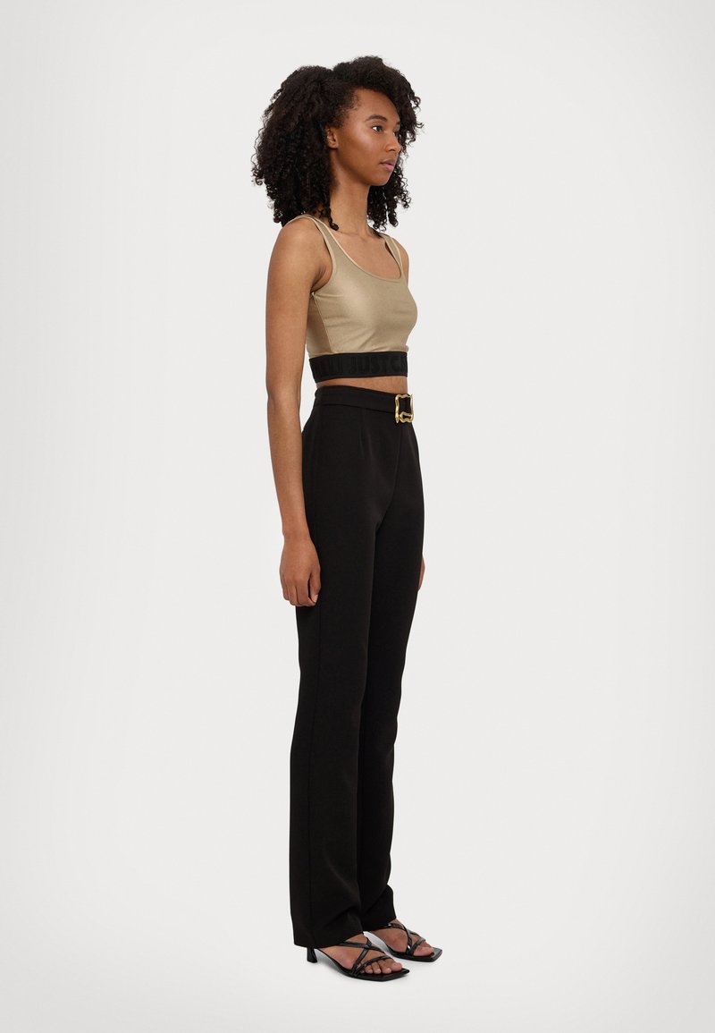 Top corto beige, pantaloni neri a vita alta con una cintura larga e fibbia dorata, e sandali neri con cinturini. Texture piatta, design elegante.