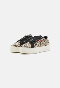 Sneakers i et beige og svart flekkete design med en hvit plattformsåle, med svarte snørebånd og en rød logoaccent på siden.