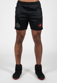 Shorts de sport noirs avec des accents rouges sur les c�ôtés, arborant un graphique gris "Est. 82" et un logo rouge. Fabriqués en tissu lisse et léger.