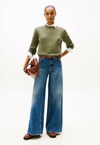 Groene gemêleerde gebreide trui, witte overhemdkraag, blauwe wijde jeans, bruine leren handtas en bruine instap-schoenen.