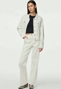 Bela denim jakna z dvema žepoma na prsih in ujemajočimi se belimi širokimi hlačami, v kombinaciji s črno kratko majico in čevlji z zebra vzorcem.