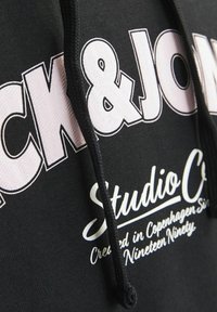 Crna kapuljača s velikim bijelim natpisima "Jack & Jones" i "Studio C", s teksturiranom tkaninom i odgovarajućim crnim vezicama.