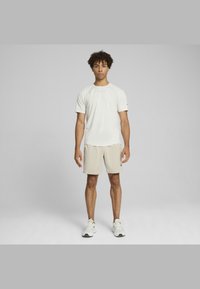 Pantalones cortos deportivos de un beige claro con un ajuste holgado, combinados con una camiseta blanca de manga corta ajustada, ambos confeccionados con un tejido transpirable. Zapatillas crema.