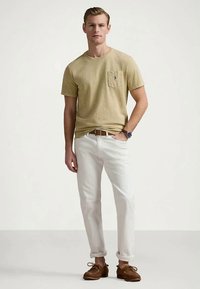 T-shirt kaki à manches courtes avec poche, associé à un pantalon blanc et des chaussures bateau marron. Design simple, coupe décontractée et matière en coton.