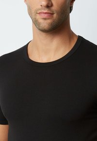 Tricou negru cu mânecă scurtă, fabricat dintr-un material de bumbac neted, având un guler clasic și o croială mulată.