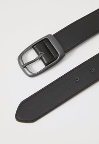 Ceinture en cuir noir avec une boucle en métal rectangulaire. Texture lisse, fermeture à ardillon et plusieurs trous d'ajustement le long de la sangle.