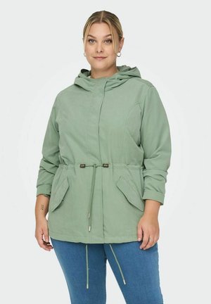 Veste à capuche vert clair avec une taille cintrée, deux poches avant et des accents avec cordons de serrage. Le tissu semble doux avec une finition légèrement texturée.