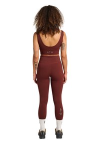 Bordeaux sport-bh och höga tights i stretchigt material. Bh:n har en rundad rygg; tightsen har logotypdetaljer nära vristerna.