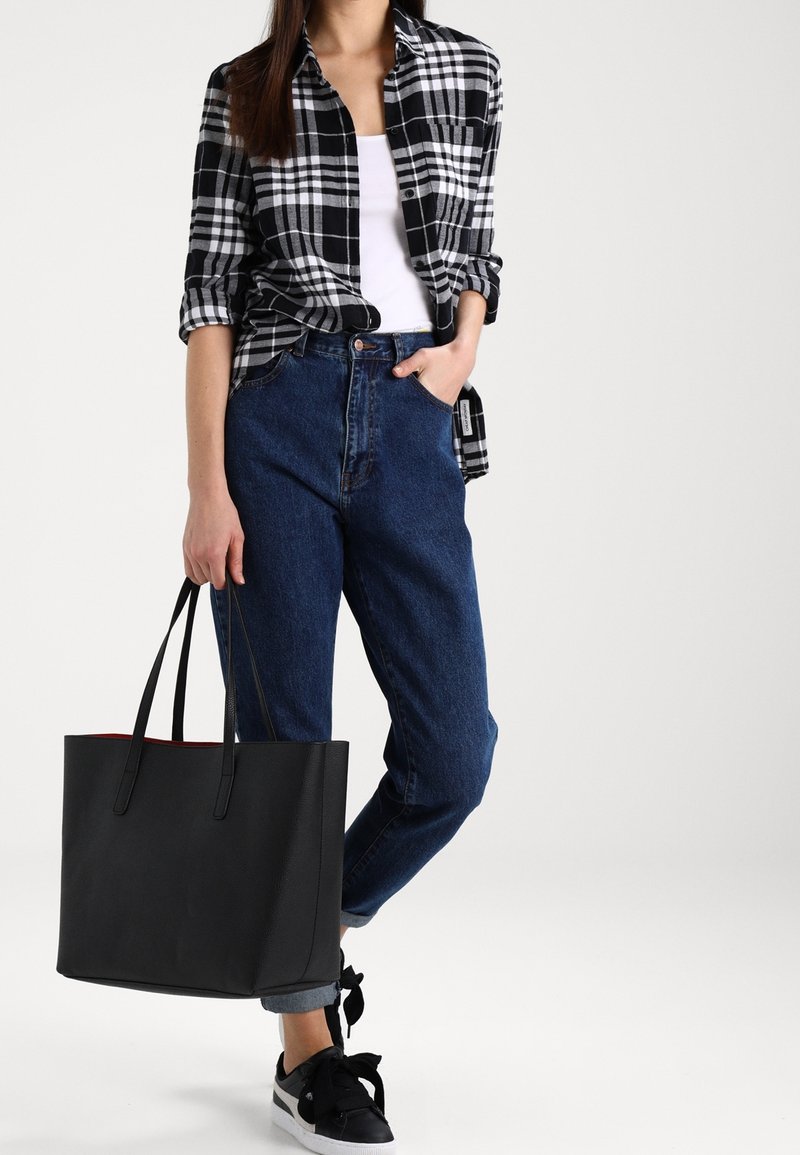 Chemise en flanelle à carreaux noir et blanc, débardeur blanc, jeans bleu taille haute, sac fourre-tout noir et baskets noires avec accents blancs.