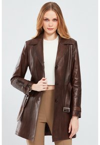 Brown leather trench coat with a tailored fit, large lapels, button closure, side pockets, and zipper details on the cuffs.