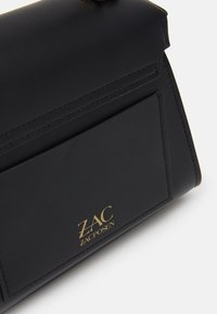 Borsa a tracolla nera in pelle con forma strutturata, dotata di un logo dorato e dettagli di cucitura. Include una tasca frontale per una maggiore funzionalità.