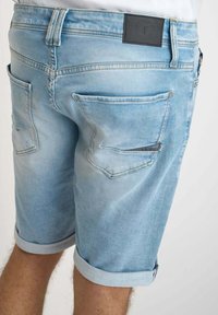 Shorts de mezclilla en azul claro con una textura descolorida, que cuentan con dobladillos enrollados, bolsillos traseros y una etiqueta de cuero en la cinturilla.