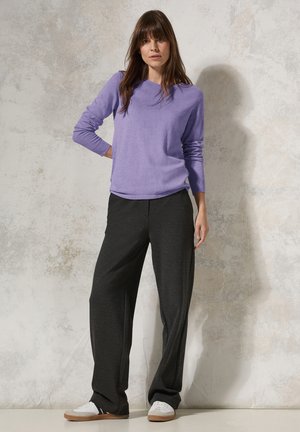 Lila Langarmoberteil kombiniert mit dunkelgrauen, weiten Hosen. Die Hosen haben eine glatte Textur, und das Ensemble wird mit weißen Sneakern abgerundet.