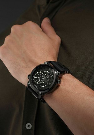 Schwarze analoge Armbanduhr mit einem strukturierten, hexagonalen Zifferblatt, drei Chronographen-Subdials und einem mattschwarzen Silikonarmband.
