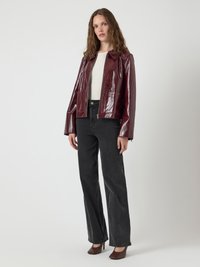 Burgundy patent leather jacket with a collared neckline, two front pockets, paired with high-waisted black wide-leg jeans and brown heels.