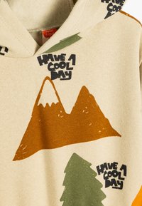 Felpa beige con grafiche di montagne e alberi in verde e arancione. Testo "Buona giornata" stampato in nero. Morbido tessuto.