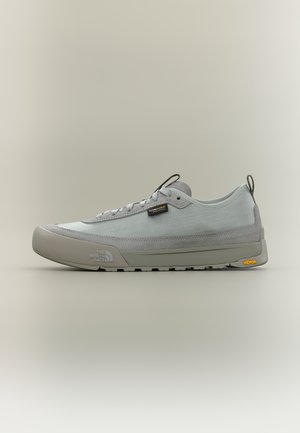 Šviesiai pilkas žemo profilio sportinis batelis su tinklelio ir zomšos viršumi, batraiščių uždarymas, The North Face ir Vibram logotipai ant pado ir šone.