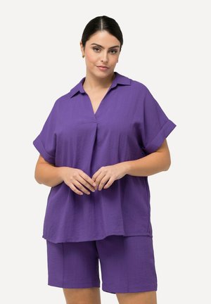 Fioletowa koszula z krótkim rękawem z kołnierzykiem i luźnym krojem, w zestawie z dopasowanymi fioletowymi szortami z lekkiego materiału.