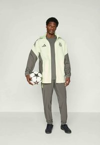 Hellgrüner und grauer Trainingsanzug mit athletischem Schnitt, bestehend aus einer weißen Reißverschlussjacke und passenden Hosen. Hält einen schwarz-weißen Fußball.