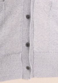 Ljusgrå cardigan gjord av mjukt stickat tyg, med en knäppt framsida med fyra mörka knappar och två detaljerade framfickor.