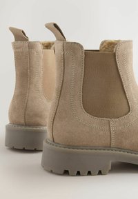 Beige velúr Chelsea csizma, elasztikus oldalsó panelek, textúrált felület, horogfülek és gumitalp jellemzi. Alacsony kivágású dizájn, mely erős tapadást biztosít.