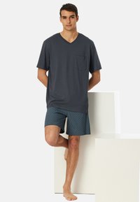 Männliches Freizeitoutfit mit einem dunkelgrauen V-Ausschnitt-T-Shirt mit Tasche und gemusterten blauen Shorts. Weicher Stoff, lässige Passform.