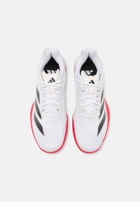 Valkoiset urheilukengät, joissa mustia ja harmaita yksityiskohtia, teksturoitu verkkopäällinen ja kirkkaan punainen ulkopohja. Nauhallinen malli, jossa logotunnelmia.