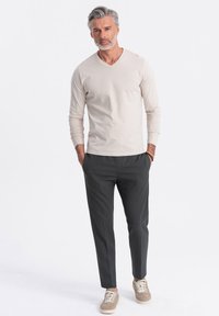 Hellbeige Langarm-V-Ausschnittshirt, kombiniert mit dunkelgrauen Hosen und beigen Sneakern mit weißen Schnürsenkeln. Schlichtes, körpernahes Design.