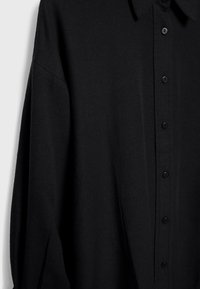 Czarna koszula na długi rękaw z zapięciem na guziki, standardowym kołnierzem, teksturowaną tkaniną i widocznymi czarnymi guzikami z przodu.