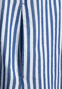 Randig tyg har växlande blå och vita vertikala linjer, med en delad detalj och en texturerad yta nära sömmen.