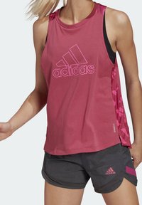 Różowy sportowy top bez rękawów z dużym różowym logo Adidas, w połączeniu z szarymi szortami z różowymi akcentami. Lekka tkanina, swobodny krój.