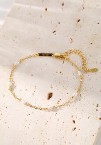 Złota bransoletka z perłami słodkowodnymi, z delikatnym wzorem łańcuszka i małym regulowanym zapięciem. Grawerowana zawieszka z napisem "AG 925".