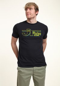 Černé bavlněné tričko s žlutou a modrou grafikou "JT Racing USA" na přední straně. Krátké rukávy a kulatý výstřih.