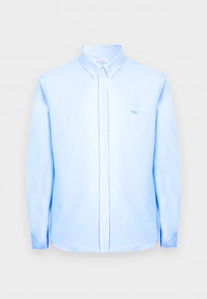 Jasnoniebieska koszula na długi rękaw z guziczkami, kołnierzykiem na guziki oraz małym logo lisa po lewej stronie klatki piersiowej.