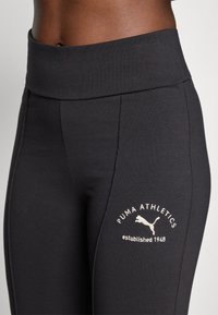 Svarta träningstights med bred midja, med en subtil logotyp i vit text och en springande katt-symbol. Mjuk, elastisk tyg.