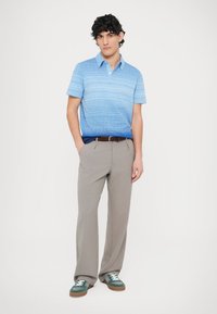 Niebieska koszulka polo w paski z kołnierzykiem, szare plisowane spodnie i zielone trampki. Koszulka ma wzór gradientowy i krótkie rękawy.