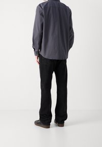 Harmaa, rento pitkähihaisen paita, jossa on napilliset kalvosimet ja pyöristetty helma, yhdistetty mustiin suoriin farkkuihin ja tummiin kenkiin.