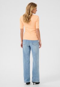 Peach ribbed top with short sleeves, paired with light blue wide-leg jeans and black heels. The outfit features a fitted silhouette and casual style.