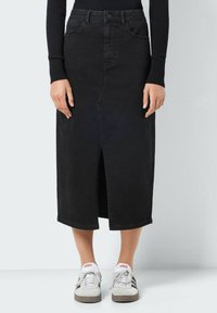 Črna denim midi krila s sprednjo zarezo, petimi žepi in klasično zasnovo pasu. Ujemajo se z belimi supergami. Gladka tekstura.