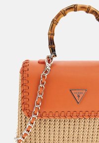 Tan vävda halmhandväska med en orange konstläderflik. Har ett bambuhandtag och ett silverkedjesnöre. Metallogotypsaccent syns.