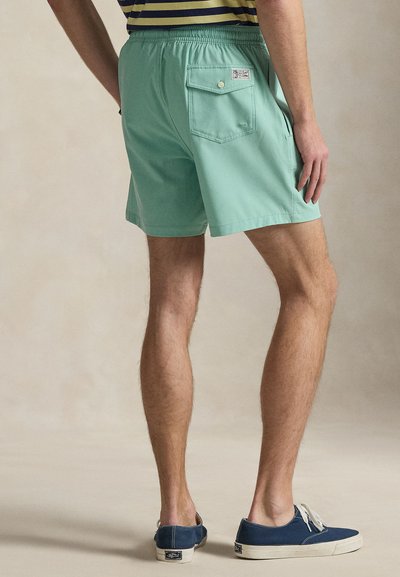 Σορτς σε μέντα πράσινο με ελαστική μέση, που διαθέτουν πίσω τσέπη και ετικέτα σε αντίθετο χρώμα· συνοδεύονται από μπλε καμβά παπούτσια.