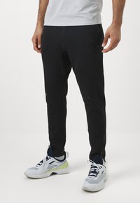 Svarta träningsbyxor med slim fit, som har en mjuk textur, diskret branding och kontrasterande sömmar. Matchas med vita och marinblå sneakers.