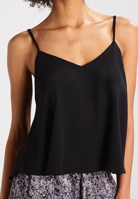 Svart ärmlös linne med tunna axelband, med en V-formad halsringning och en löst sittande design av lätt tyg.