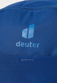 Tessuto blu con il logo "deuter" in azzurro, con texture liscia e un design pulito e snello. I dettagli includono cuciture lungo i bordi.