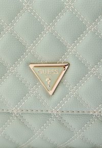 Geantă matlasată verde mentă, realizată dintr-un material texturat, cu un logo triunghiular auriu cu detalii în relief și cusături contrastante.