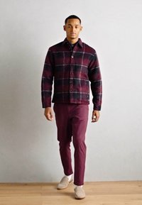 Veste à carreaux bordeaux et noir, en mélange de laine, avec une fermeture à boutons et deux poches latérales. Associée à un pantalon bordeaux.