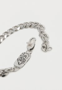 Ασημένιο βραχιόλι αλυσίδα με κούμπωμα σε σχήμα αστακού και εγχάρακτο ορθογώνιο φυλαχτό με αφηρημένο σχέδιο προσώπου.