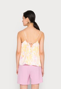 Top leveiro com padrão floral em amarelo pastelo e rosa, com alças finas e um detalhe nas costas em forma de coração. Combinado com calções rosa.